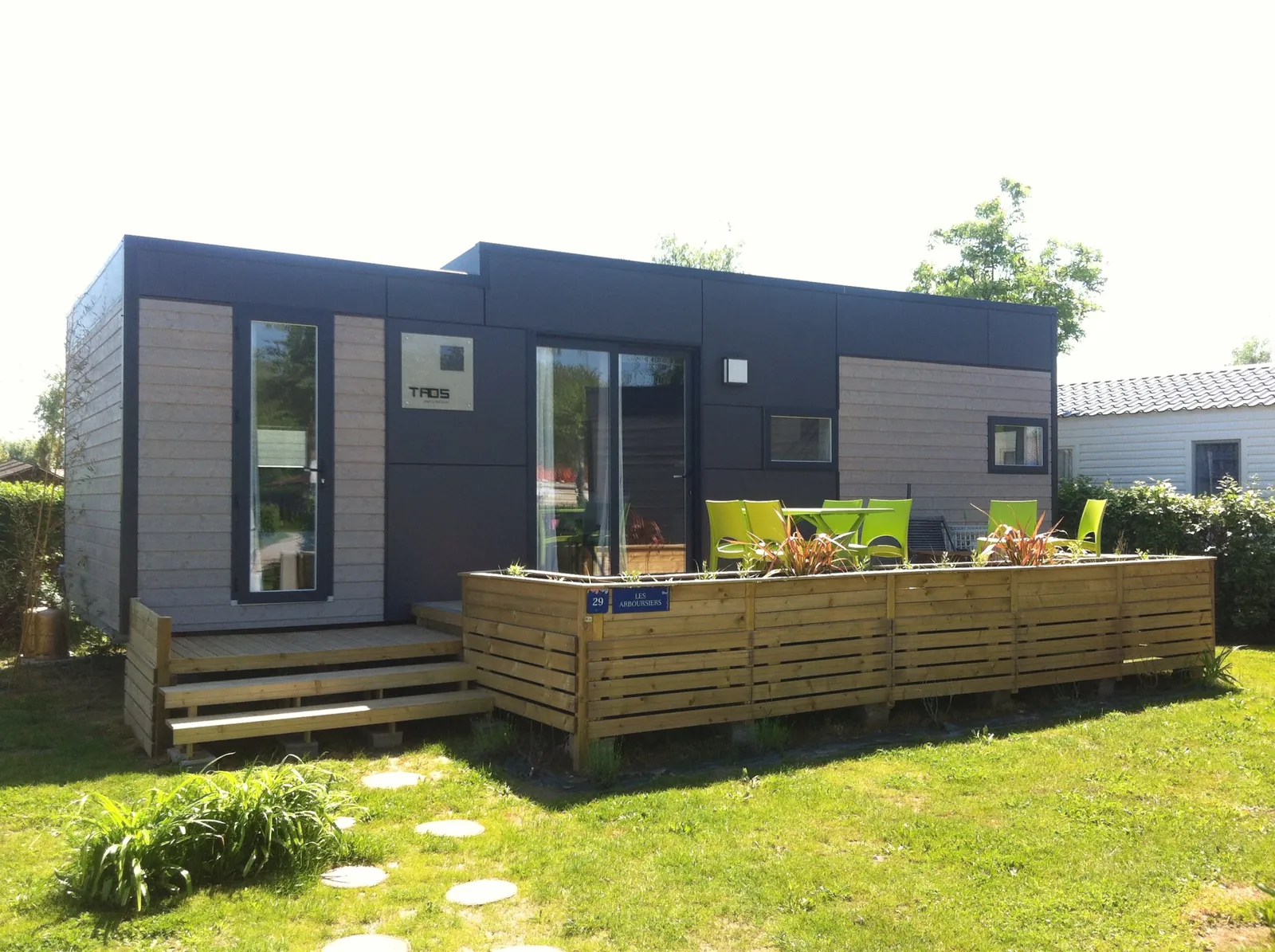 Terrasse en bois formant podium devant un mobil-home contemporain gris, avec bardage à claire-voie et mobilier de jardin