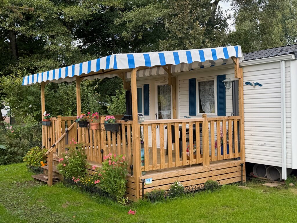 Mobil-home avec terrasse en bois couverte Deckit et bâche à rayures bleues et blanches au Camping Les Aulnes, à Bezinghem