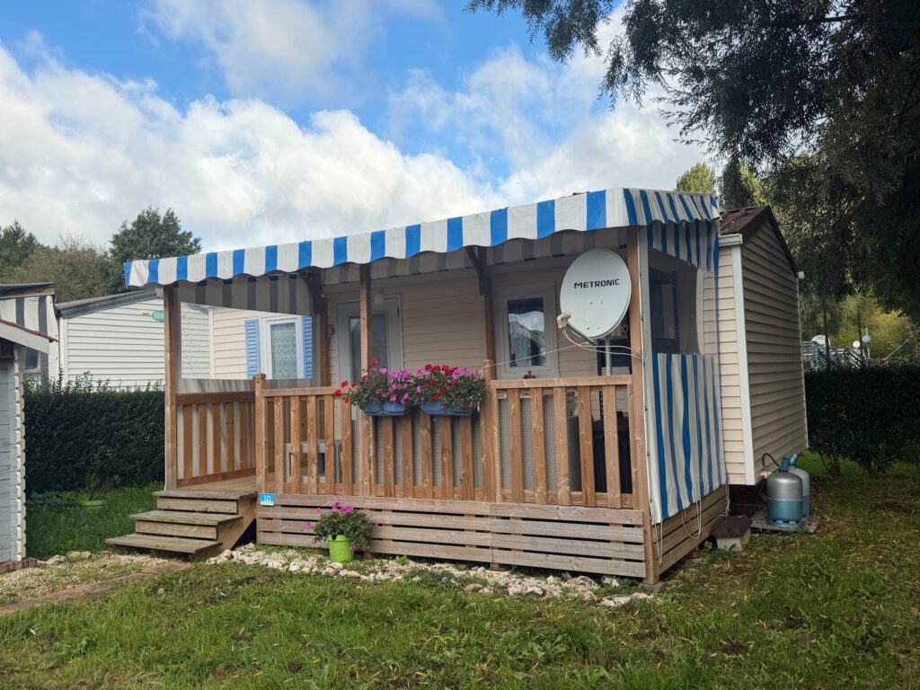 Terrasse en bois couverte Deckit avec bâche à rayures bleues et blanches et rideau latéral au Camping Les Aulnes, à Bezinghem