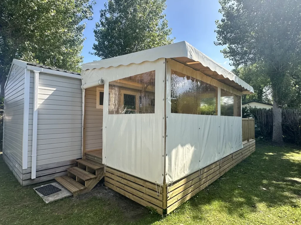 Joue et façade coulissantes en bâche vanille avec fenêtres panoramiques sur une terrasse de mobil home
