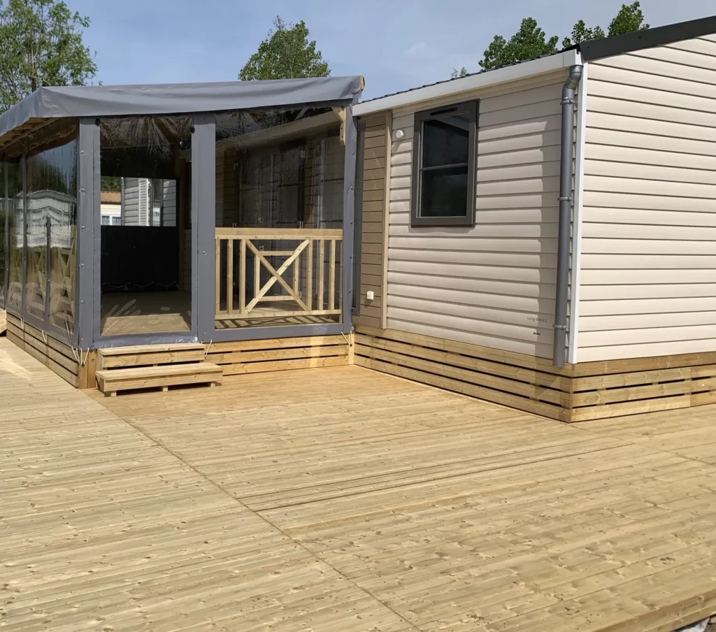 Terrasse de mobil home couverte d’une bâche grise unie, fermée par des panneaux transparents