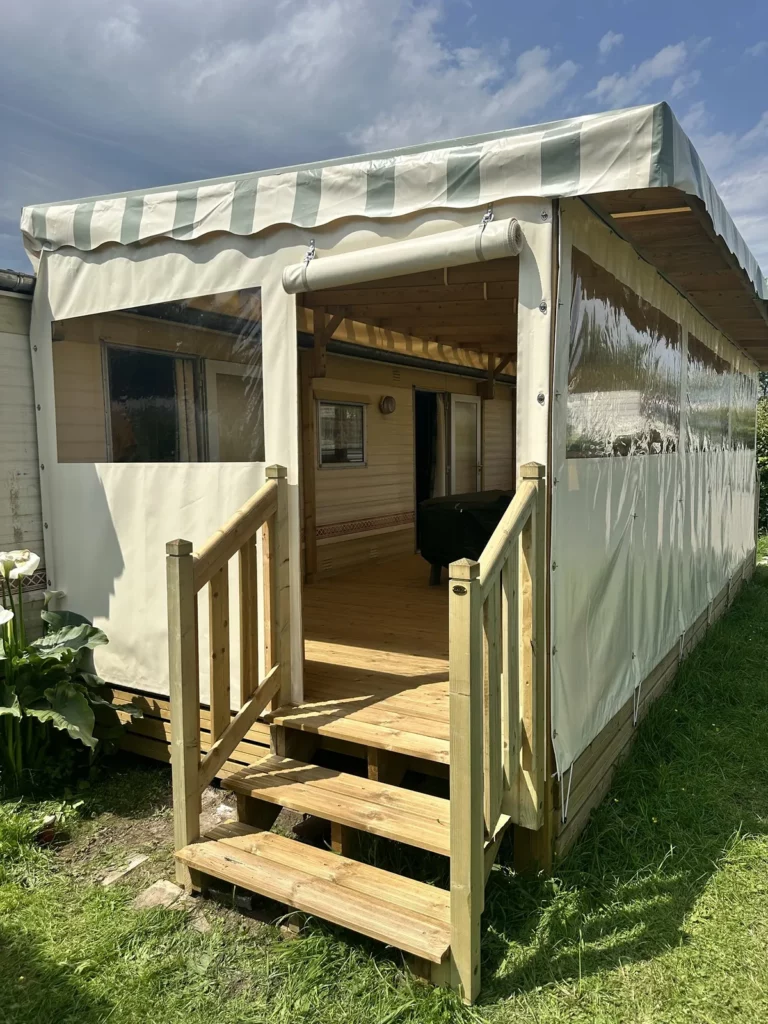 Terrasse de mobil home couverte et fermée : bâche de toit rayée vert pastel, joues et façade avec fenêtres