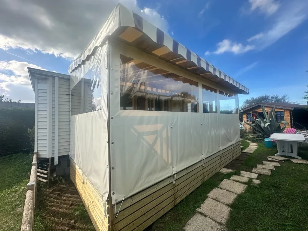 Terrasse de mobil home fermée : bâche de toit Bordeaux pastel rayé, joues et façade vanille avec fenêtres panoramiques